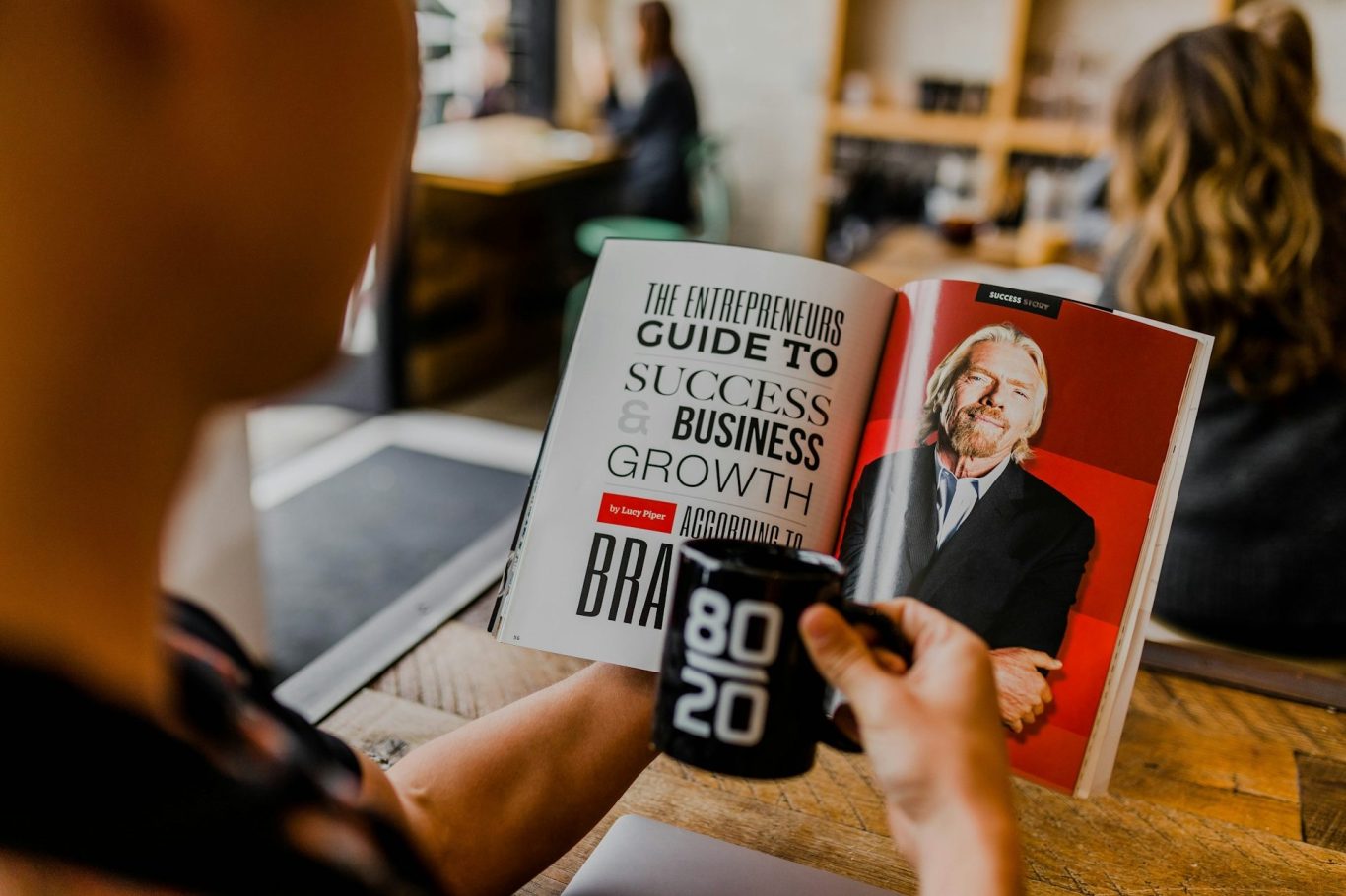 Kreative Social Media & Audio Kampagnen Eine Person hält eine Tasse und liest ein Magazin über Erfolg und Wachstum.